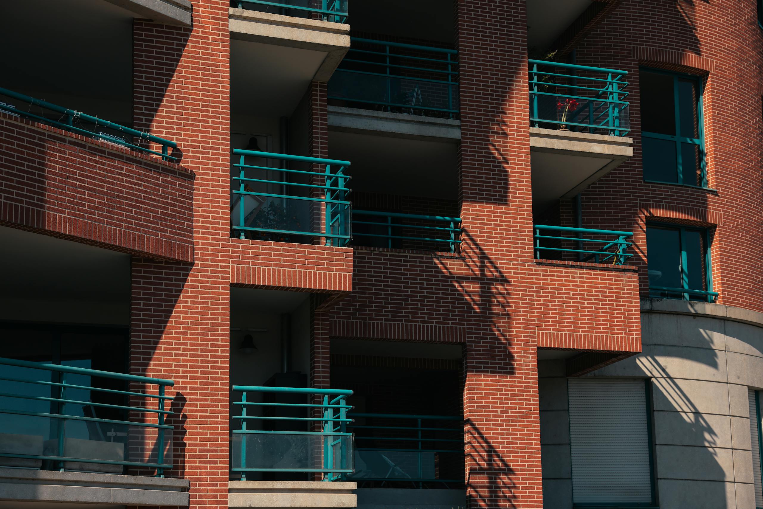Close-up of a contemporary red brick apartment building facade with green railings in Toulouse, France.